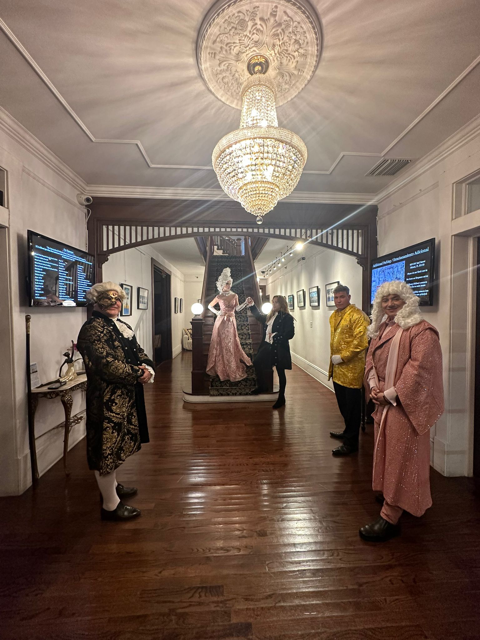 Guests in Victorian costume in a chandelier-lit hallway